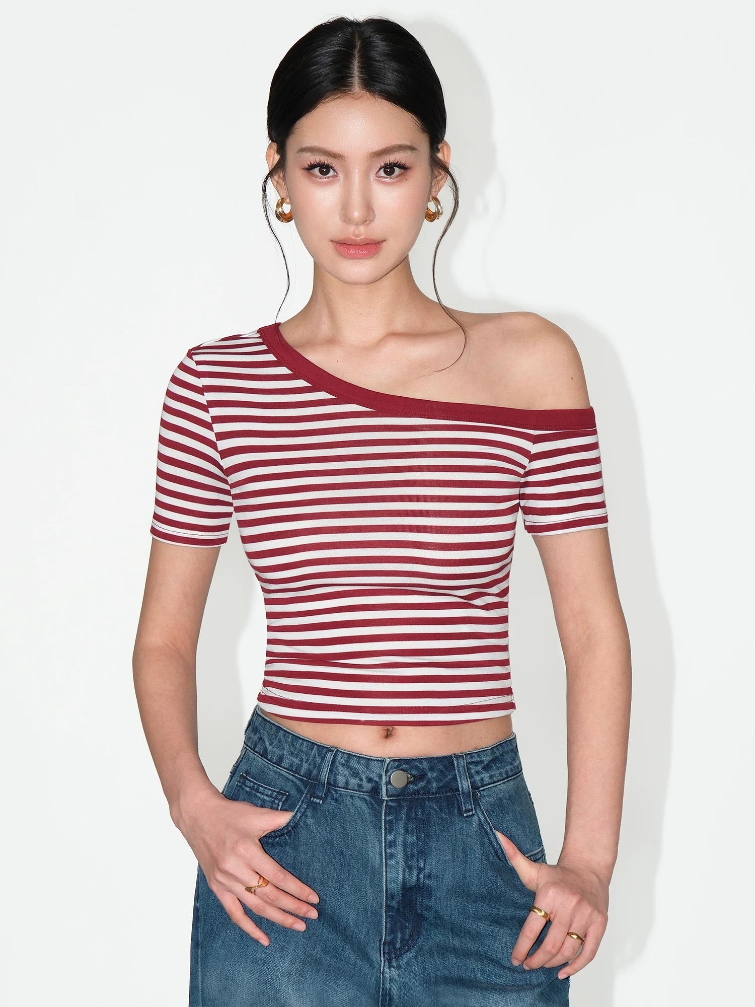 Woman wearing a red and white striped top with blue jeans on a plain background