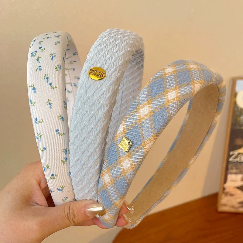 Three patterned headbands held by a hand against a neutral background