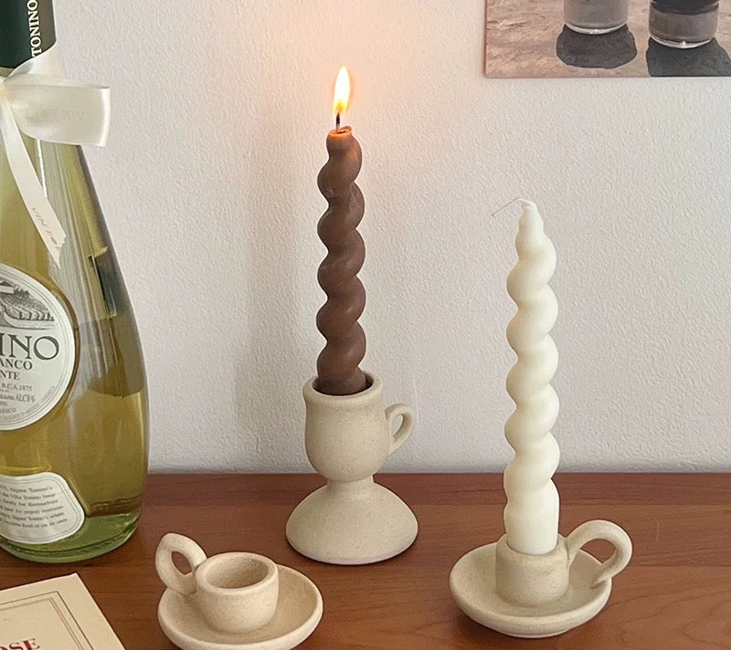 Ceramic candle holders with twisted designs on a wooden surface, next to a bottle of wine and a book.