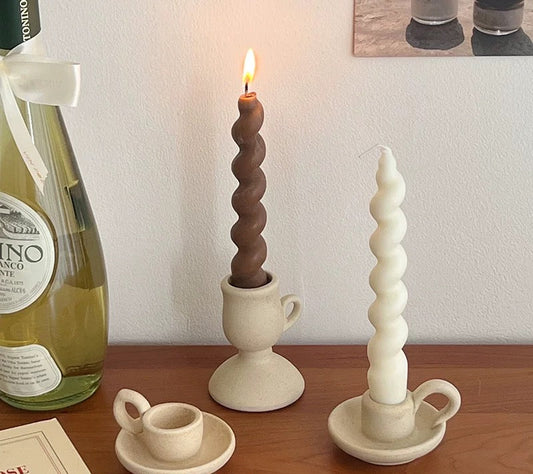 Ceramic candle holders with twisted designs on a wooden surface, next to a bottle of wine and a book.