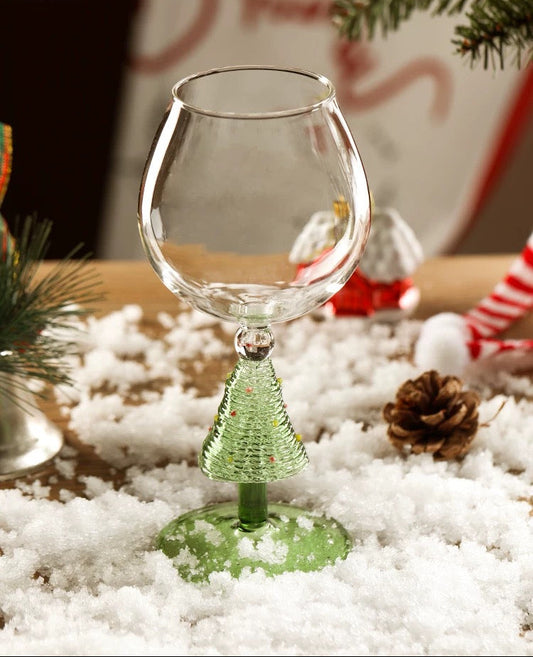 Clear glass wine glass with green base on a snowy surface, Christmas decorations in the background