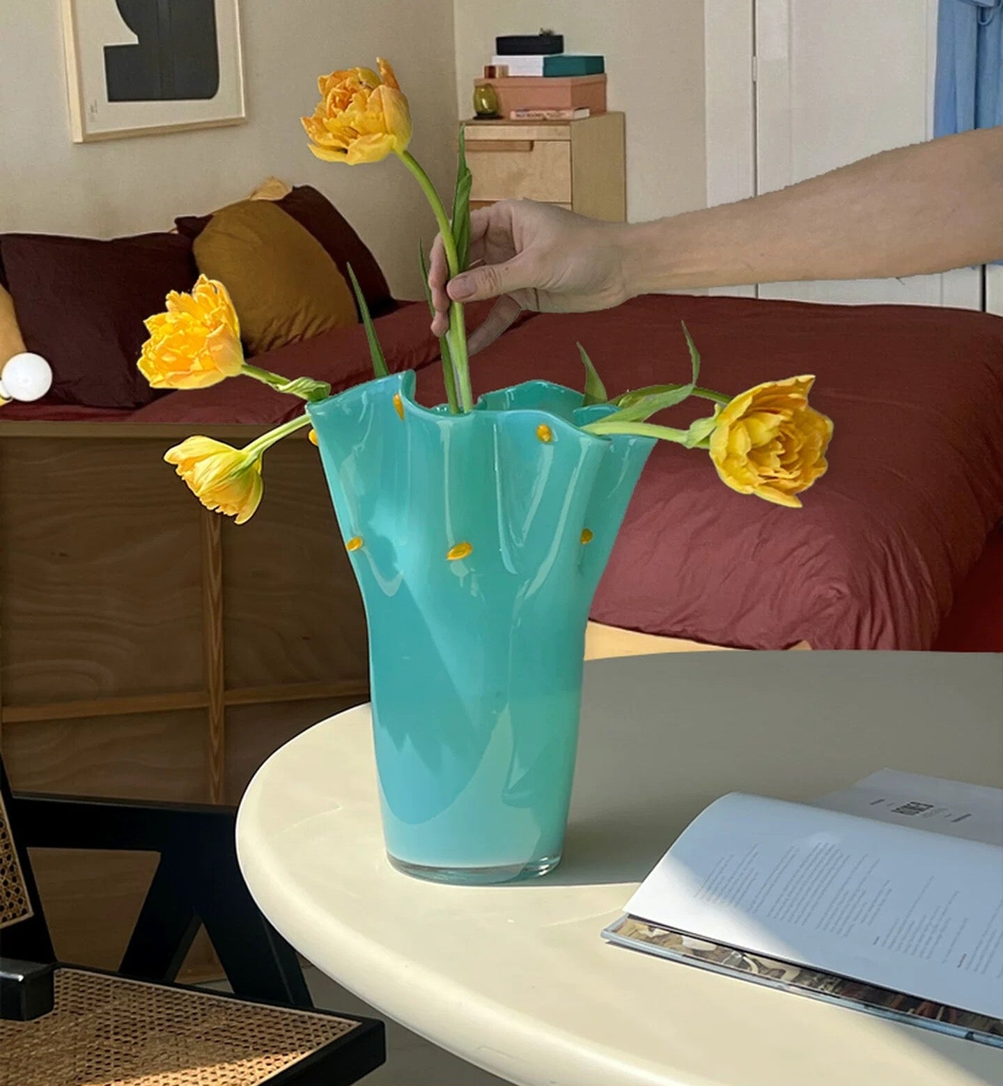 Hand placing yellow flowers into a blue vase on a table in a living room.