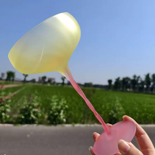 Yellow and pink object held by a hand with a blurred green field and blue sky in the background