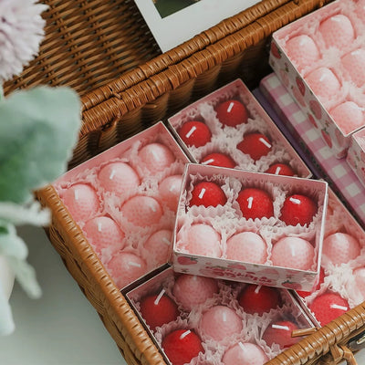 Assorted small candles in decorative boxes on a wicker surface.