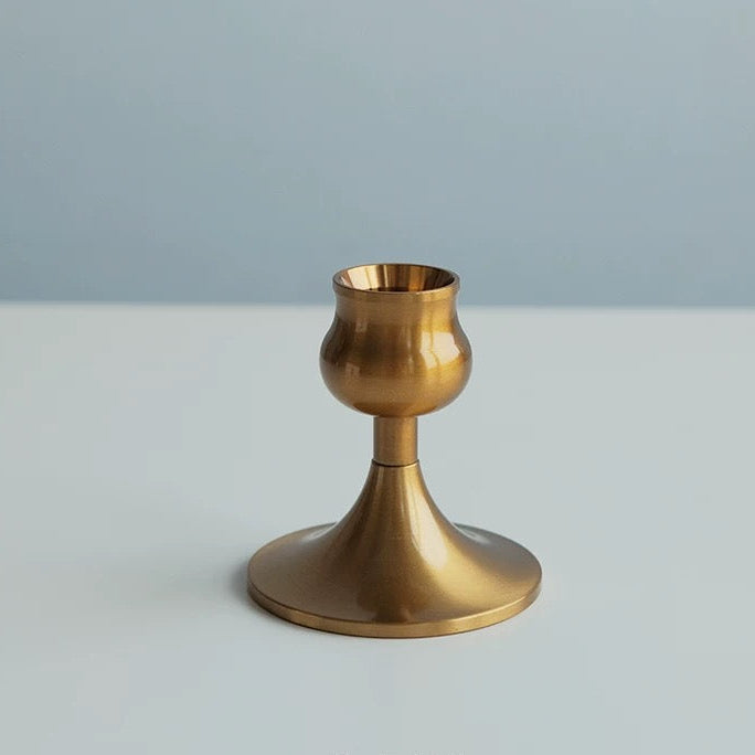 Gold candle holder on a white surface with a gray background
