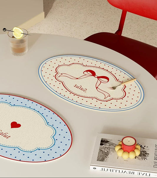 Two decorative placemats with heart designs on a table with a red chair and candle.