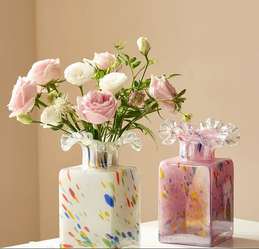 Two colorful glass vases with flowers on a beige background