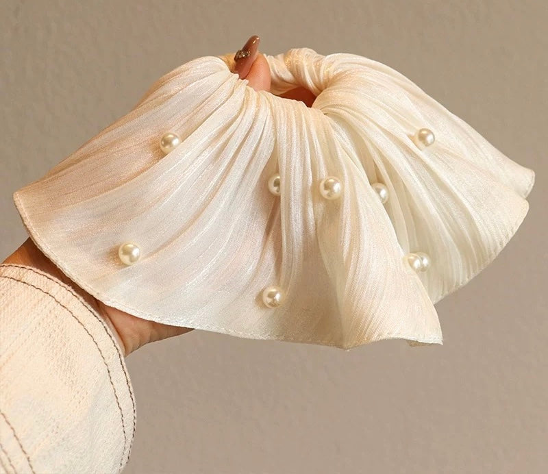 Cream-colored fabric with pearl embellishments held by a hand against a neutral background