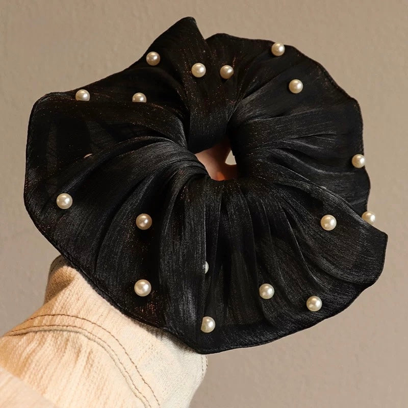 Black scrunchie with pearl embellishments on a neutral background