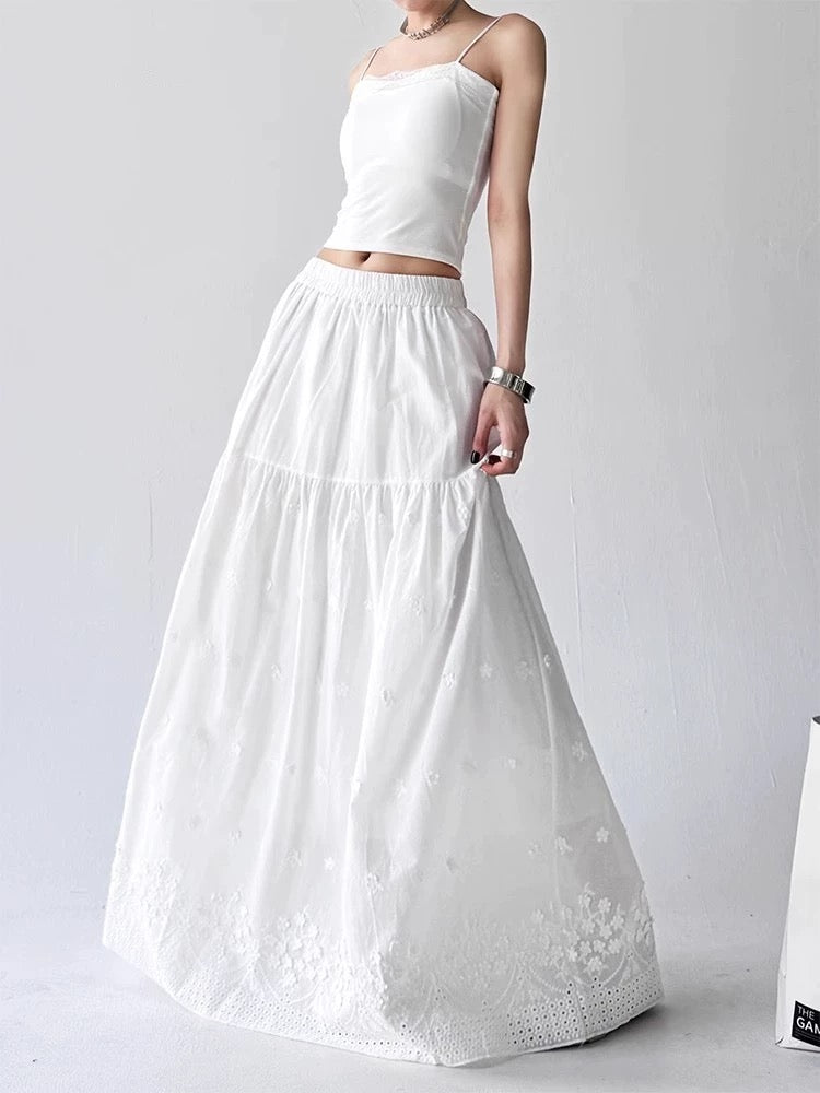 White one-shoulder top and long skirt with floral embroidery on a plain background