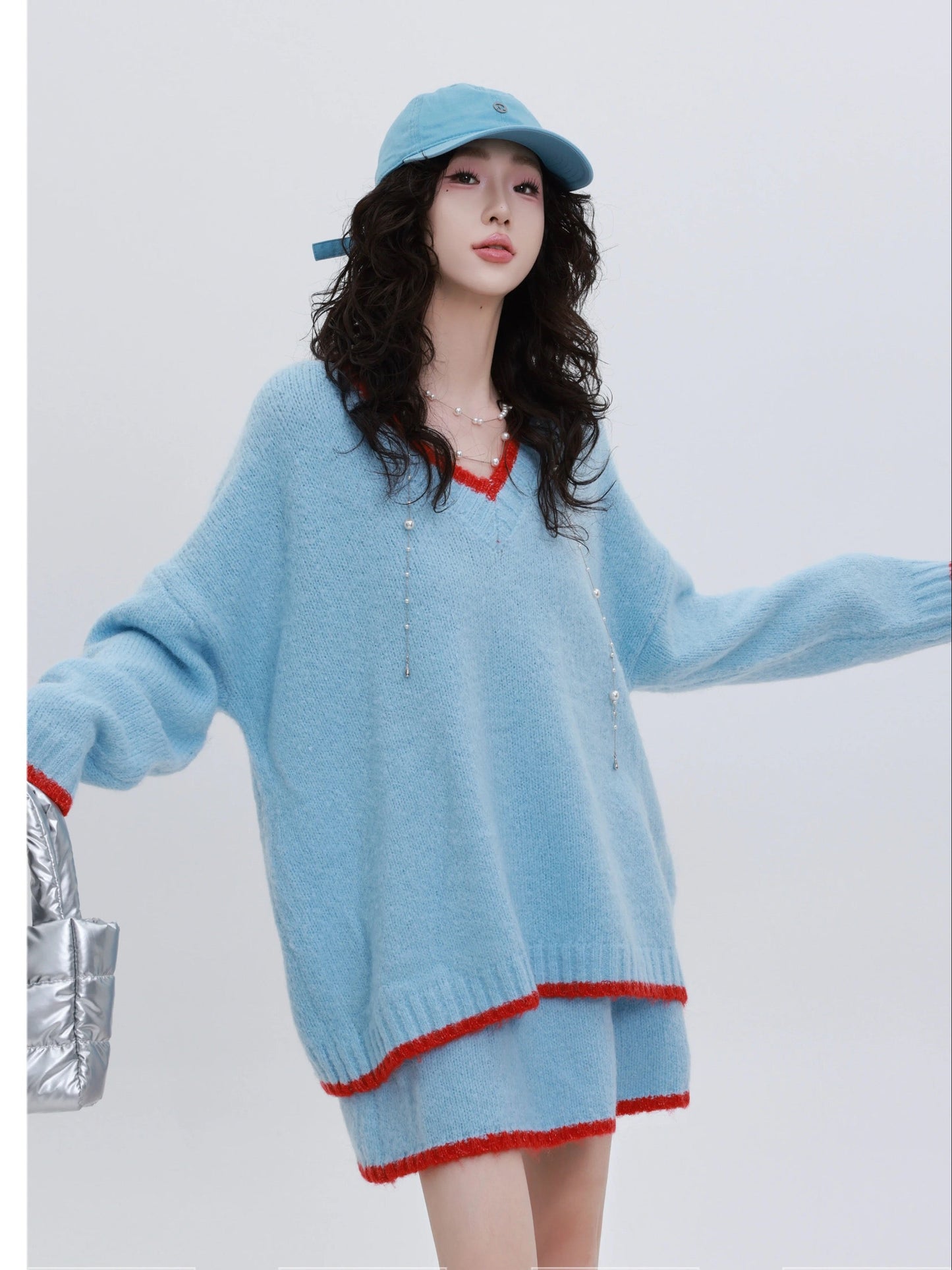 Woman wearing a light blue sweater with red trim and a matching skirt, holding a silver bag on a white background. Text indicates 'YINGZI Collection' and '2025 SS New Arrival'.