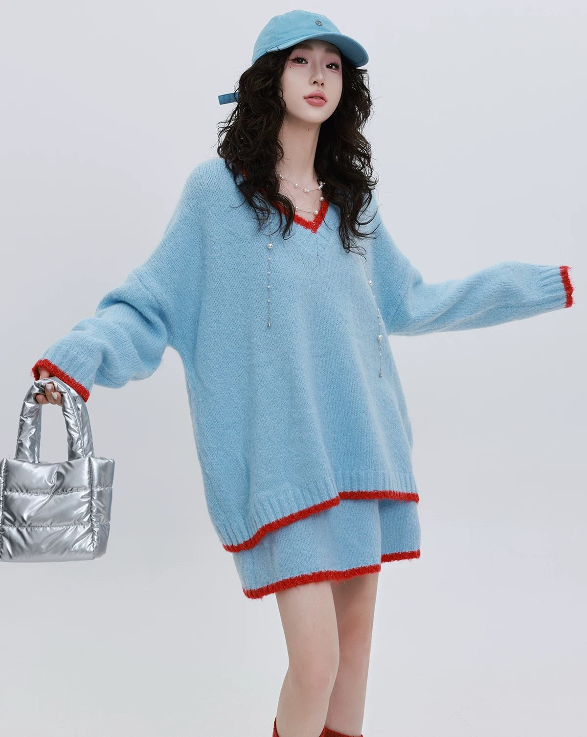 Woman wearing a light blue sweater with red trim, holding a silver handbag on a white background