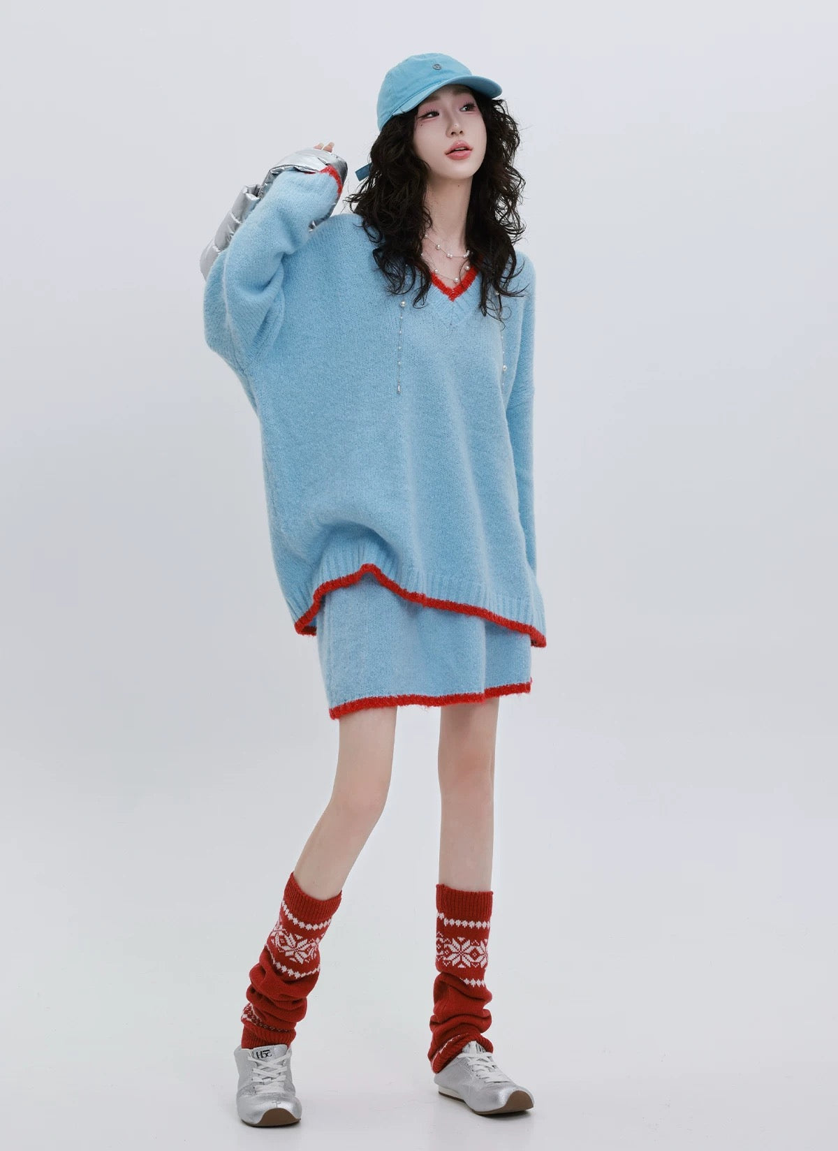 Person wearing a light blue oversized sweater with red trim, red patterned socks, and a matching cap on a white background.