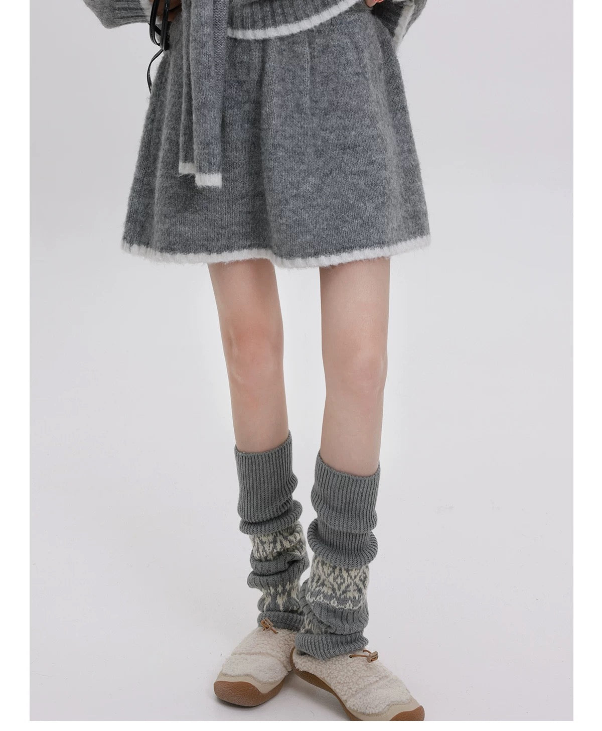 Person wearing gray knitted leg warmers and a gray coat on a white background