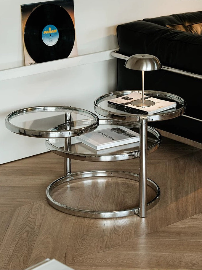 Modern silver side table with glass shelves in a living room setting.