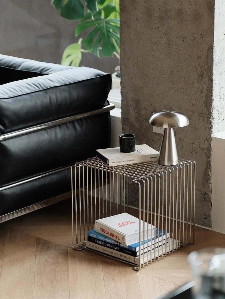 Modern side table with books and a lamp next to a black leather sofa in a room with concrete wall.