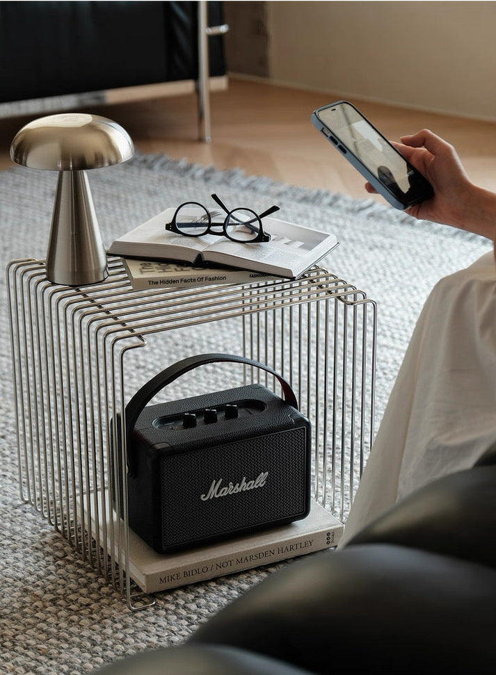Person using a smartphone with a Marshall speaker and glasses on a table in a living room.