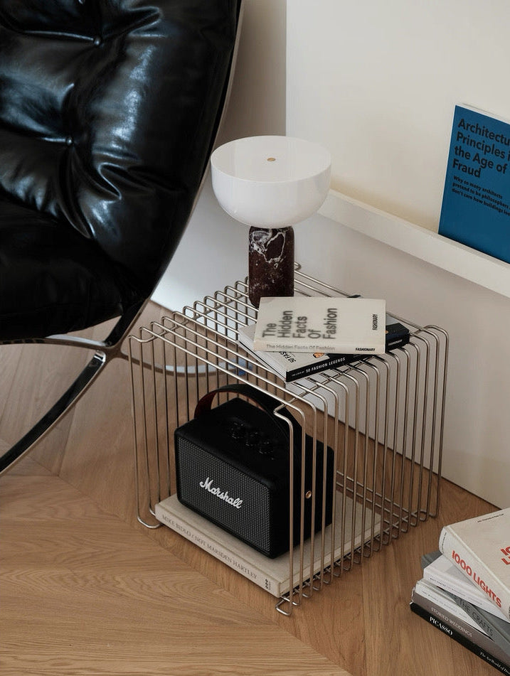 Wire magazine rack with books and a Marshall speaker on a wooden floor.