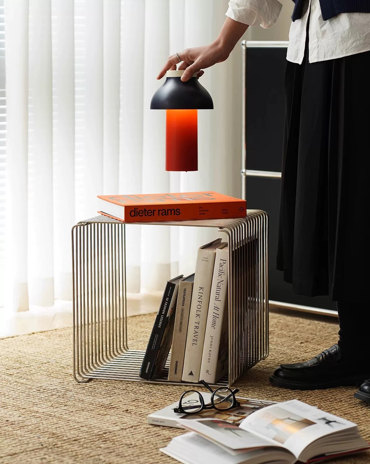 Person holding a lamp over a stack of books on a metal side table.