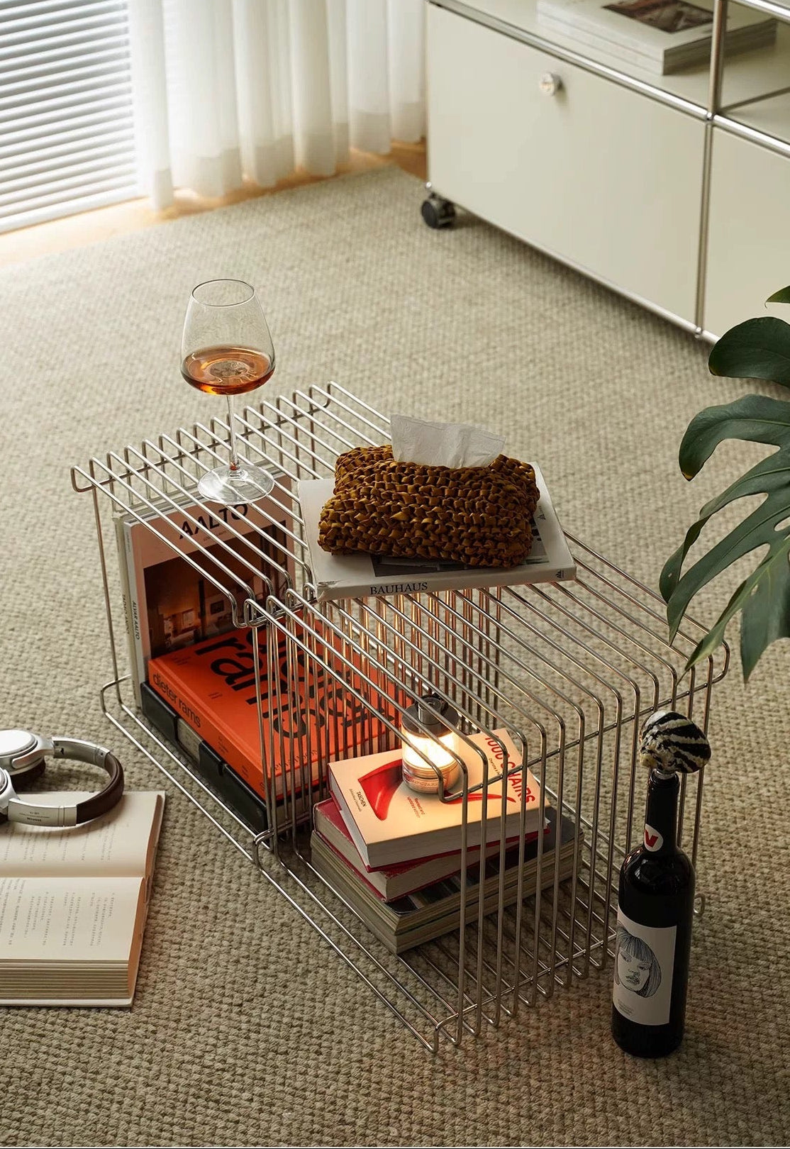 Wire pet crate used as a coffee table with books, a glass, and a bottle inside a modern living room.