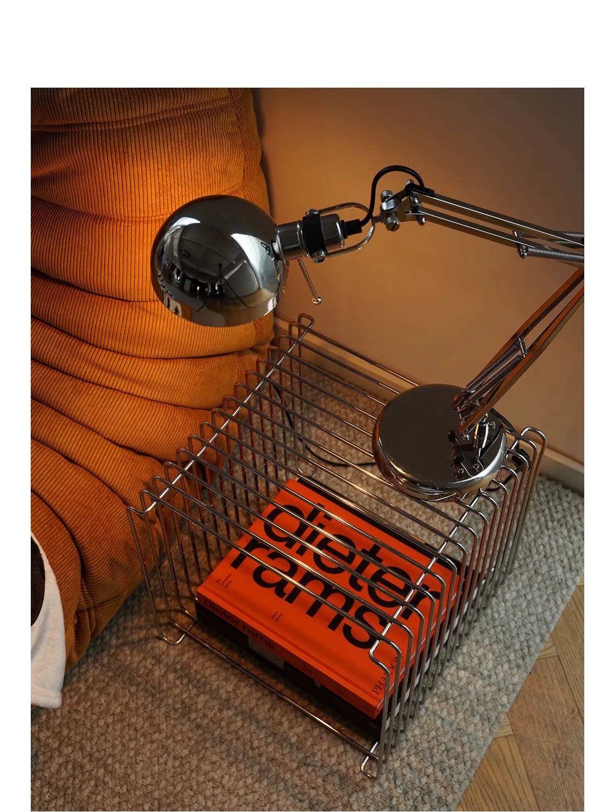 Two metal desk lamps on a wire basket with an orange book titled 'Dietrich Bonhoeffer' on a carpeted floor.