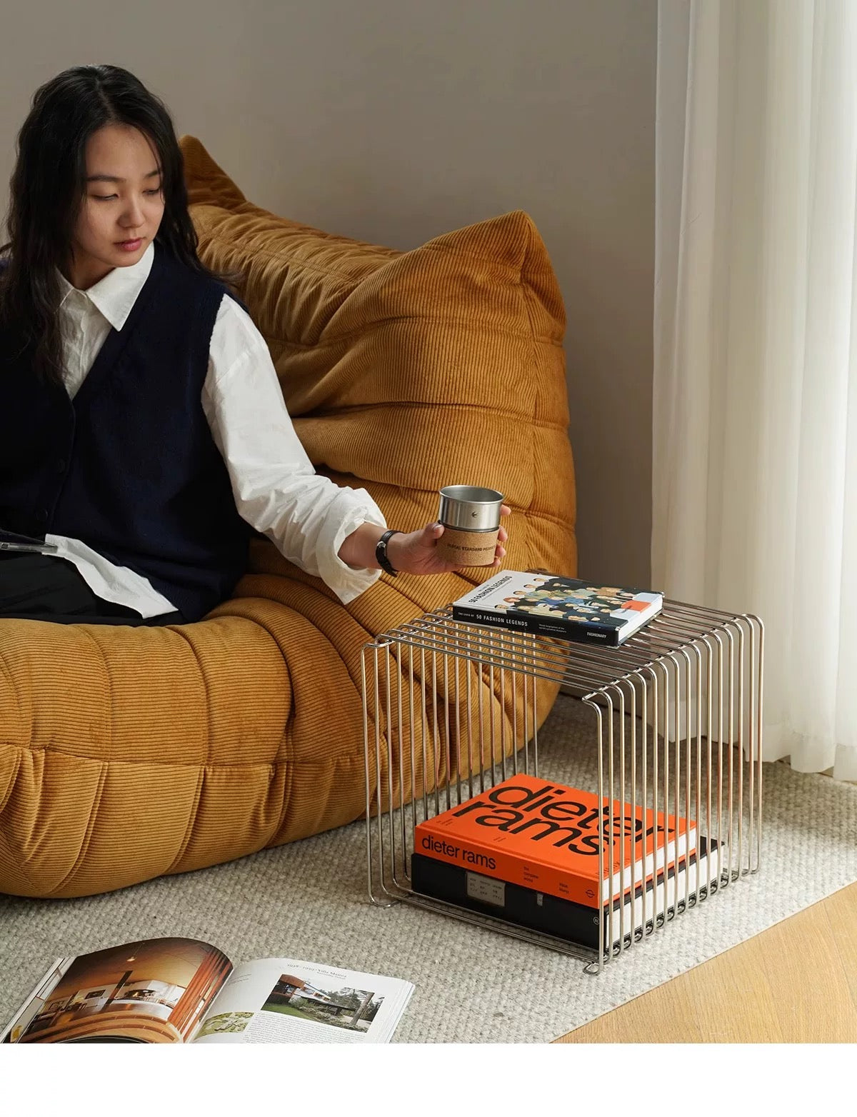 Person sitting on a mustard yellow bean bag chair holding a cup, with a small metal table next to them.