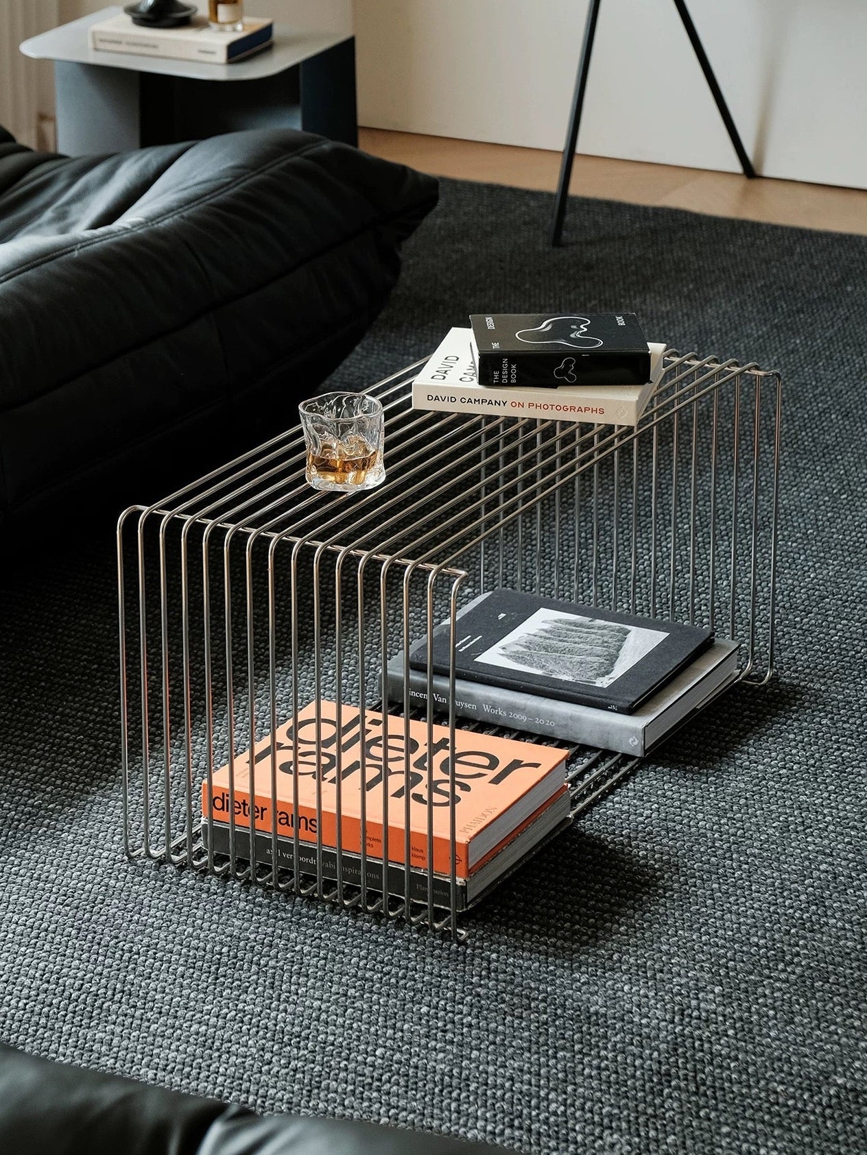 Modern wire coffee table with books and a glass in a living room setting.