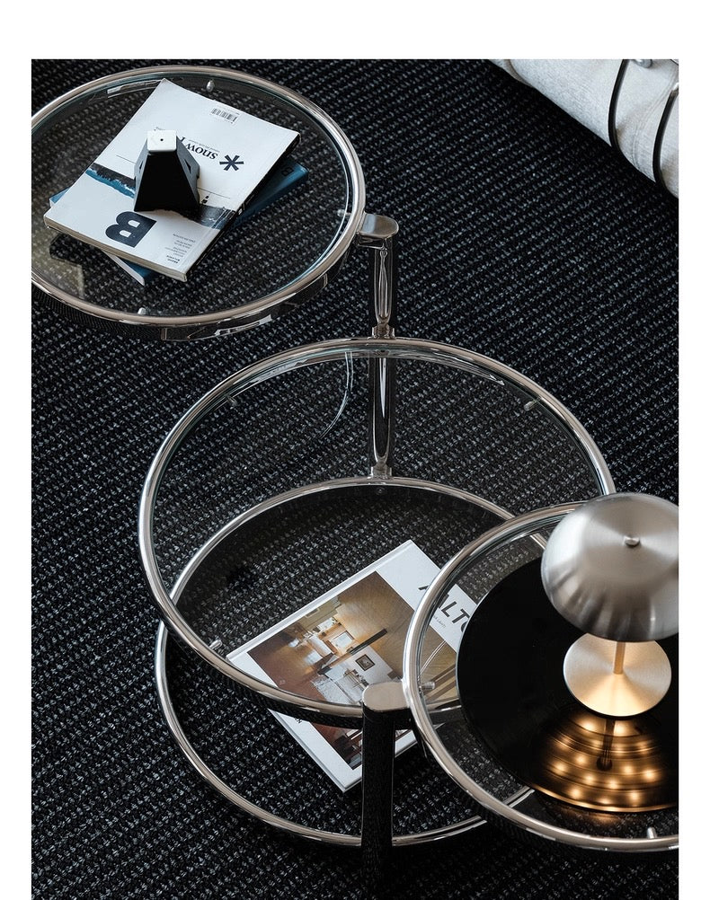 Set of three round glass tables with metal frames on a textured black surface.