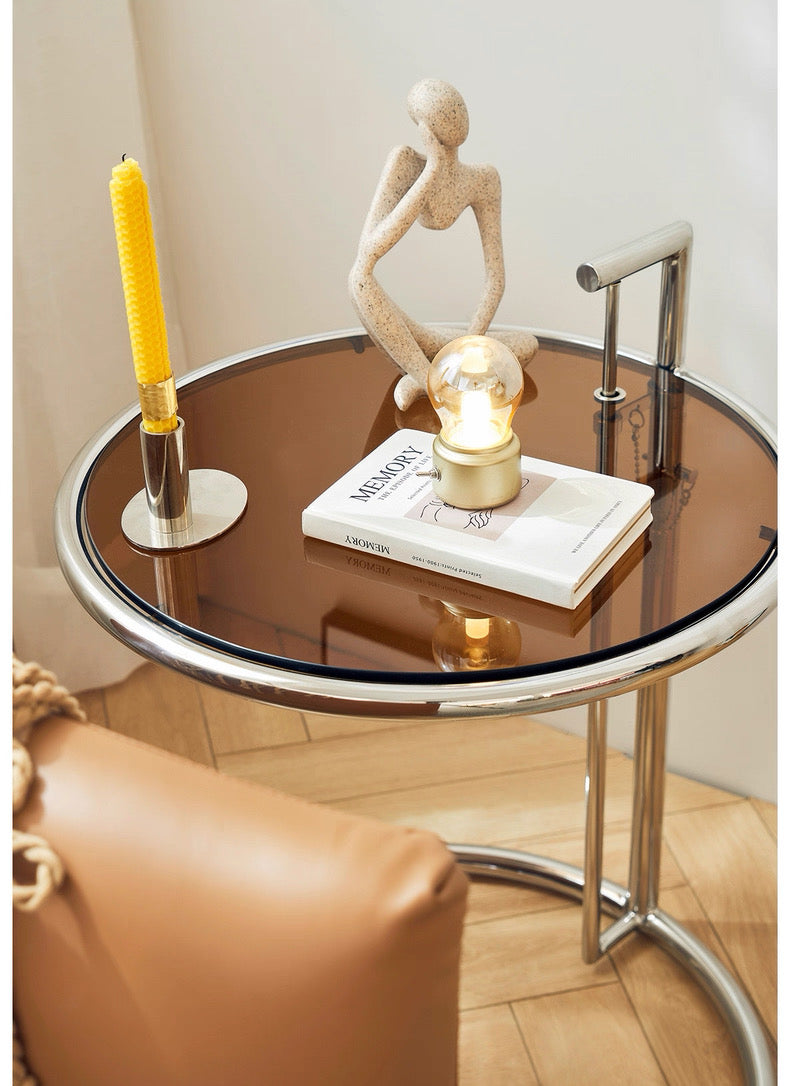 Round glass table with decorative items including a candle and sculpture in a room.