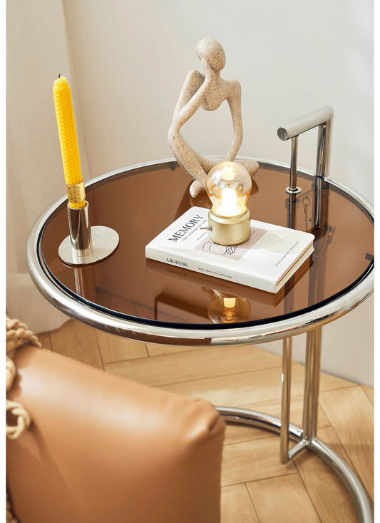Round glass table with decorative items including a candle and sculpture in a room.