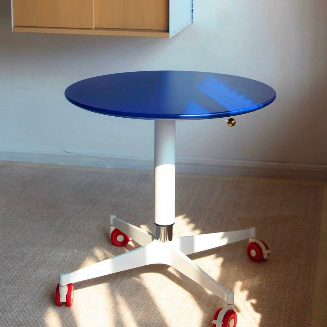 Blue round table with white base and red wheels on a carpeted floor.