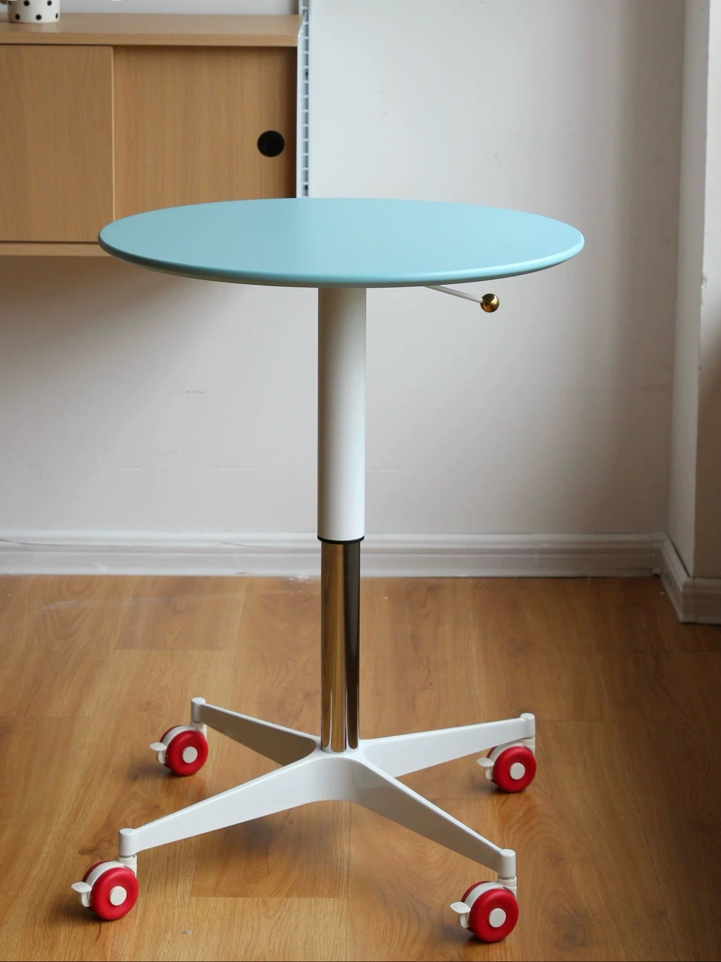 Round table with a light blue top and white base on wheels in a room setting.