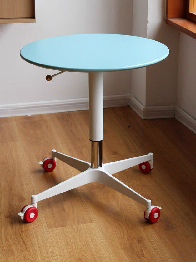Round table with a light blue top and white base on wheels in a room with wooden flooring and a window.