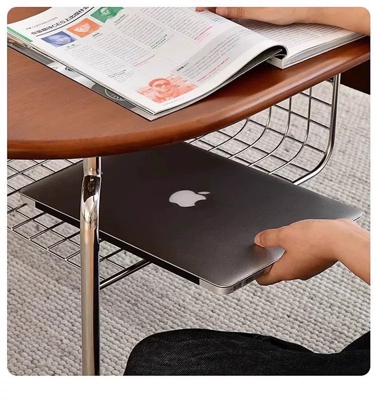 Person using a laptop under a wooden table with a newspaper on it.