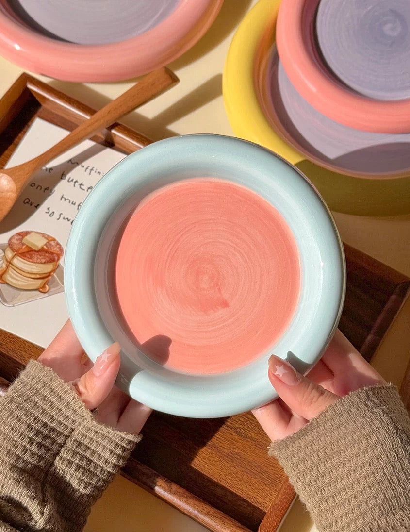 Person holding a pink ceramic dish with a textured surface, surrounded by other colorful ceramic items.