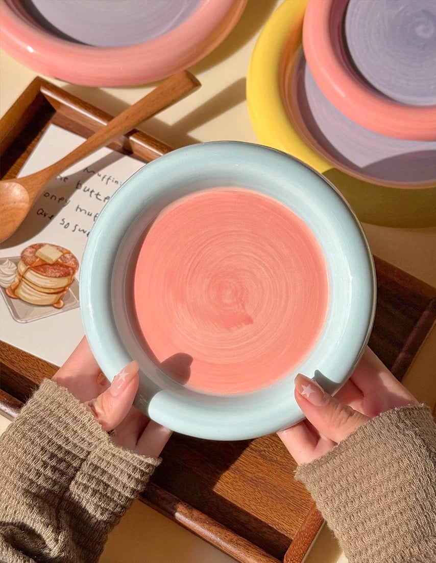 Person holding a pink ceramic dish with a textured surface, surrounded by other colorful ceramic items.