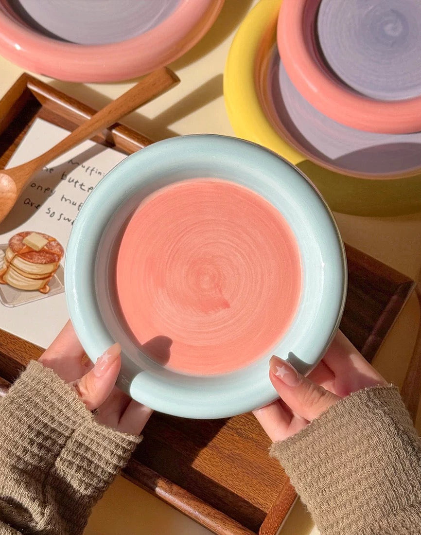 Person holding a pink ceramic dish with a textured surface, surrounded by other colorful ceramic items.
