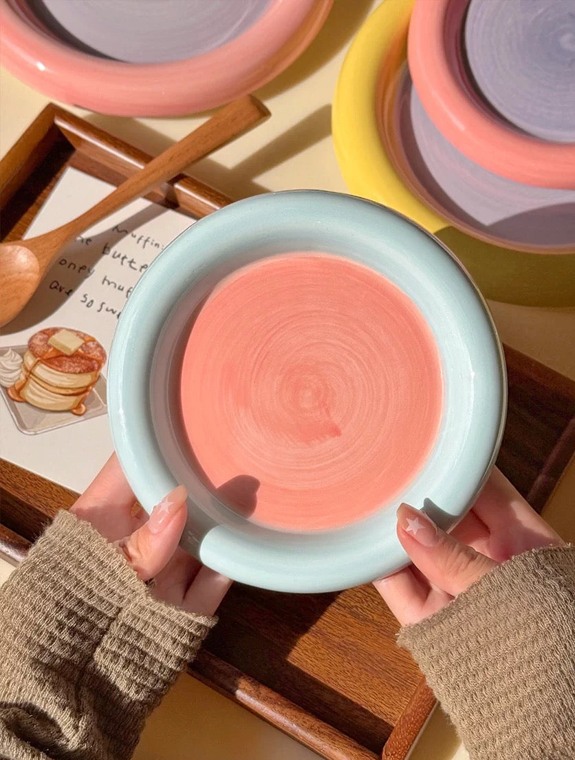 Person holding a pink ceramic dish with a textured surface, surrounded by other colorful ceramic items.