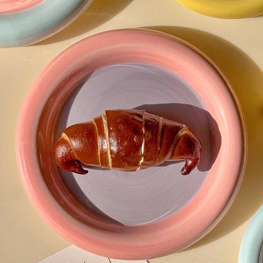 Pink ceramic plate with a croissant-shaped dessert on a yellow background
