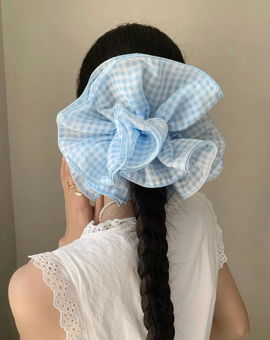 Person wearing a large blue checkered scrunchie with a plain background