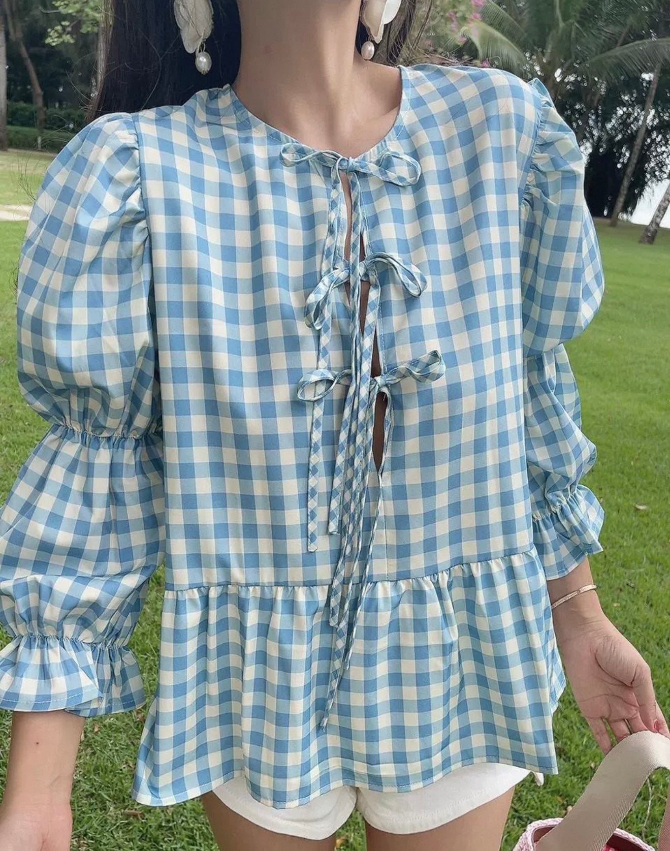 Person wearing a blue and white checkered blouse outdoors on a grassy area.