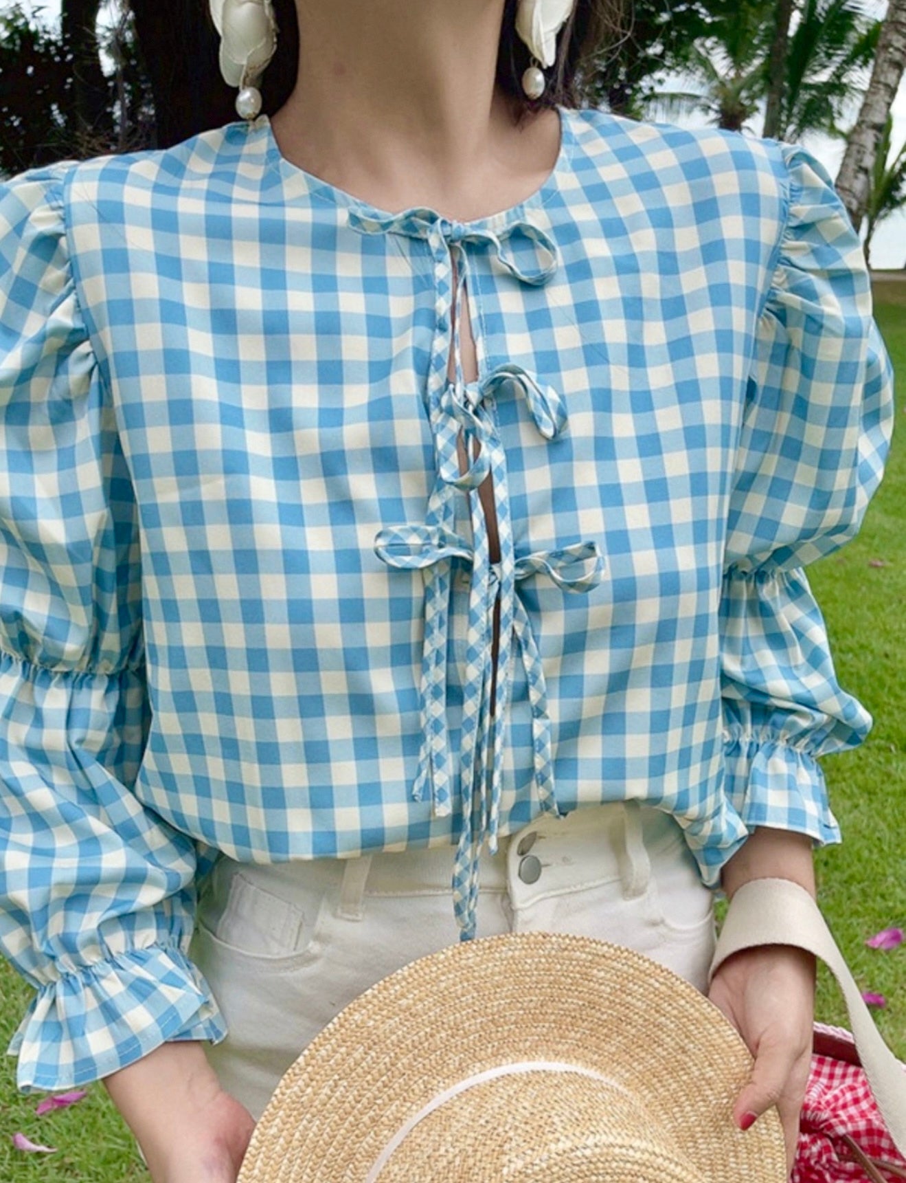 Person wearing a blue and white checkered blouse with a straw hat on a grassy background