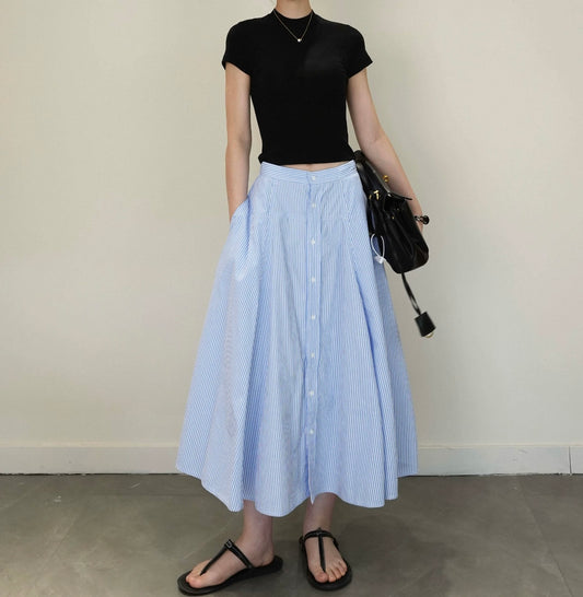 Person wearing a black top and blue striped skirt holding a black bag against a plain background