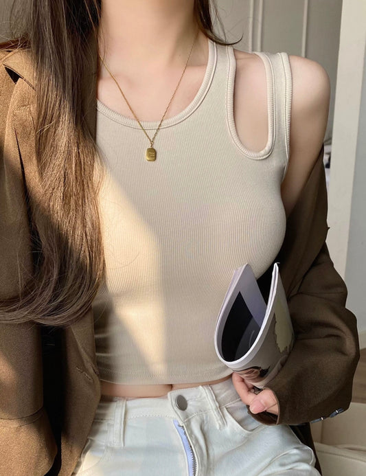 Person wearing a beige tank top and holding a white object indoors