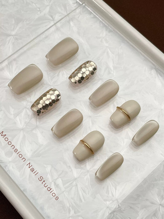 Set of beige nail art designs with gold accents on a white tray, branded 'Moonston Nail Studios'.