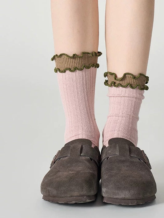 Pink socks with ruffled cuffs and brown loafers on a light gray background