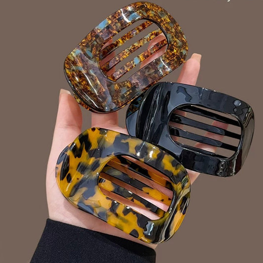 Three decorative hair bars with tortoiseshell and black designs held in a hand against a brown background.