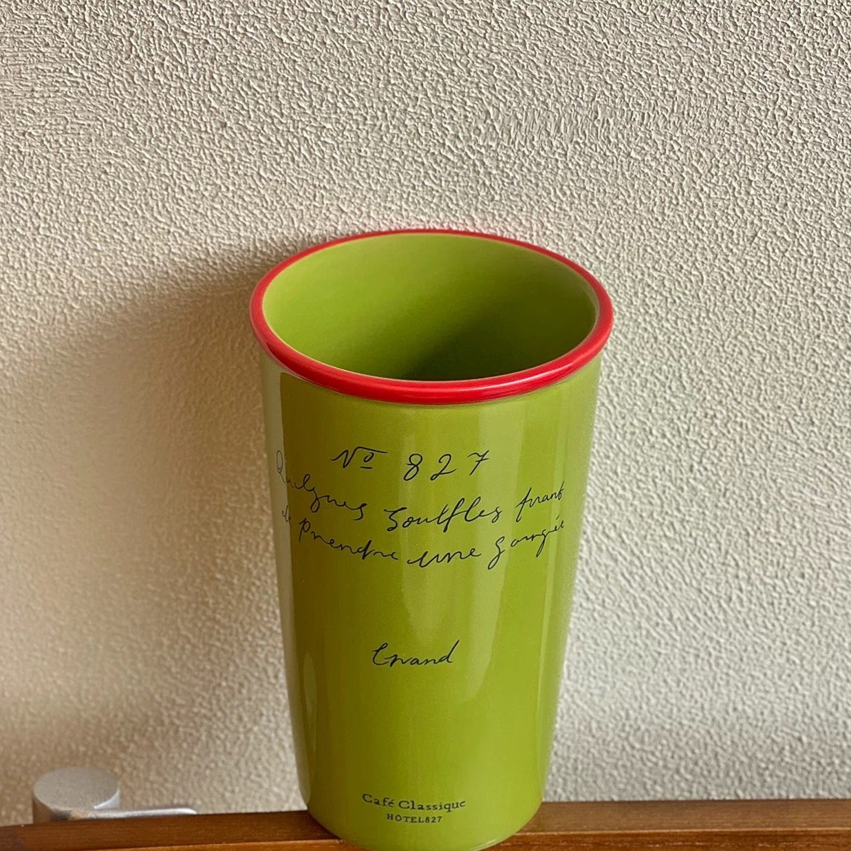Green cup with red rim on a wooden surface against a textured wall