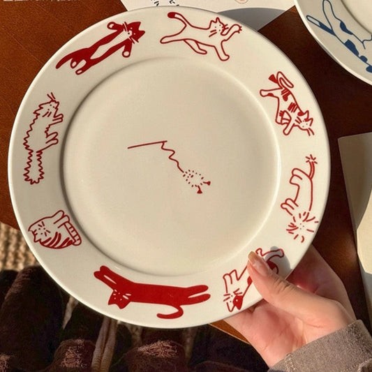 White plate with red cat illustrations held by a hand on a brown surface