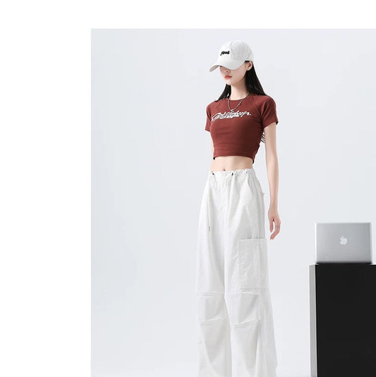 Person wearing a red crop top and white pants with a white cap, standing in front of a white wall.